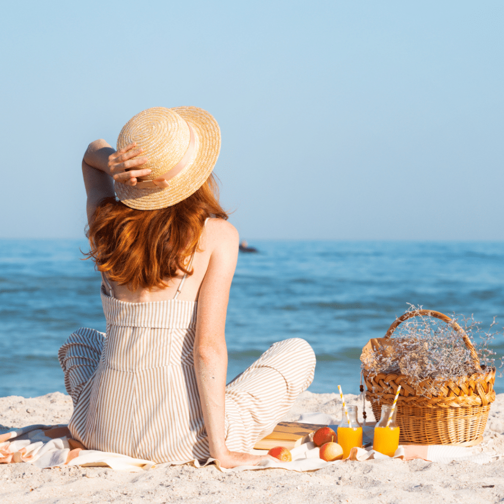 Back of a woman with hat sitting on the sand looking at the beach view